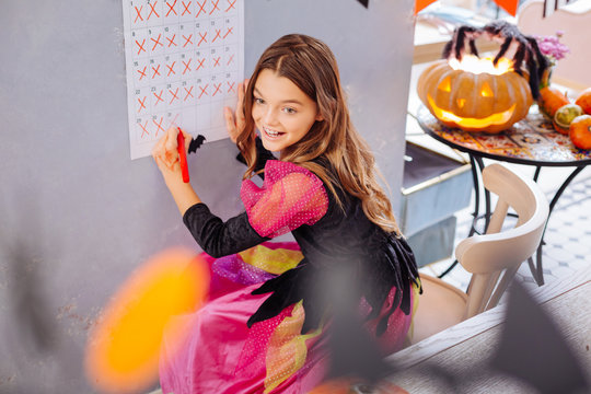 Wall calendar. Funny fashionable girl wearing pink and black Halloween dress standing near her wall calendar