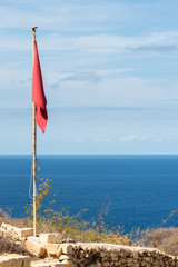 Fototapeta premium Red flag on a pole. Clouds and sea view background. Vertical. No wind