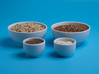 brown rice, buckwheat, flax and oat flakes in white cups on a blue background