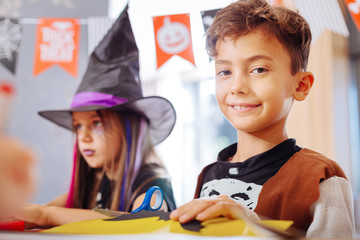 Playing in kindergarten. Cute diligent dark-haired boy wearing Halloween costume playing with other children in kindergarten