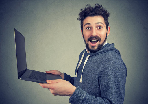 Surprised young man with laptop computer looking at camera