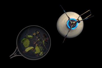 Gas burner and a bowler hat with tea from forest berries on a black background