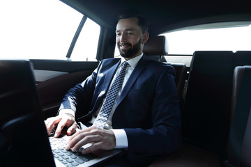 Fototapeta na wymiar businessman sitting in the back-seat of a car, using his laptop