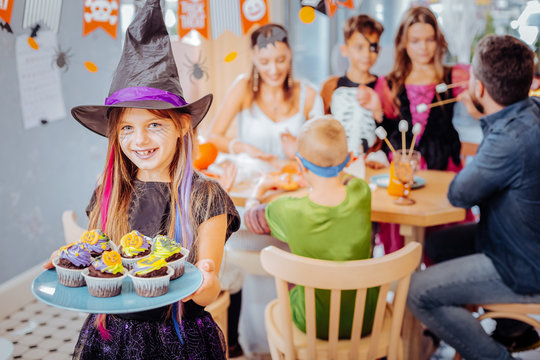 Wizard hat. Smiling girl wearing Halloween wizard hat holding plate with celebration cupcakes on the occasion of birthday