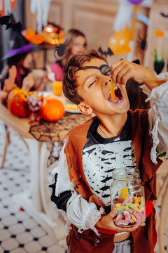 Schoolboy at Halloween. Cute schoolboy wearing nice pirate costume eating gummy worm while attending Halloween party