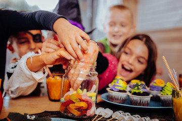 Eating sweets. Children wearing funny costumes celebrating Halloween in kindergarten laughing while eating sweets