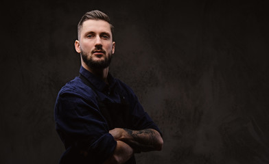 Chef dressed in shirt and apron posing with crossed arms on a dark background.