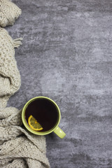 Cup of tea with lemon in hands, knitted scarf near, at gray background