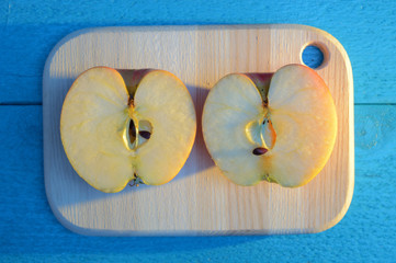 apple cuted in half on a wooden board on turquoise table with a long blue shadow