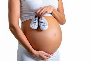 Schwangere Frau hält kleine Babyschuhe auf ihrem Bauch, isoliert auf weißem Hintergrund