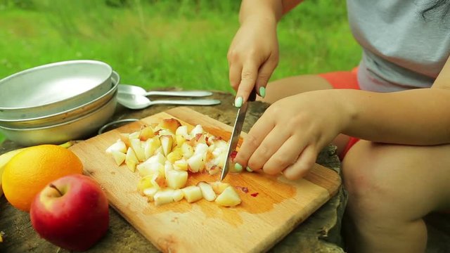 Female hands cut pieces of peach on a wooden board for a salad on a picnic.