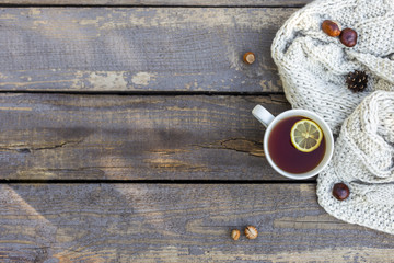 tea in tea cup with lemon, knitted scarf, nuts and cone near at wood background