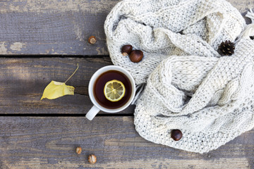 tea in tea cup with lemon, knitted scarf near at wood background