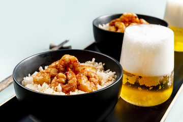 Fried shrimp and rice in a black bowl. Glass with beer. The background is gray.