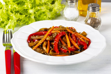 Vegetable salad. Aubergines fried, pepper, carrots on a white plate. The concept of healthy eating. White wooden background. Copy space