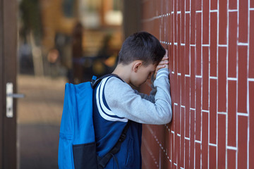 Schoolboy cries in the yard of the school leaning against the wall