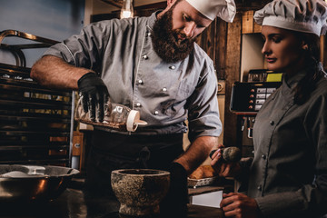 Chef pours sesame into a mortar. Cooking lesson in bakery.