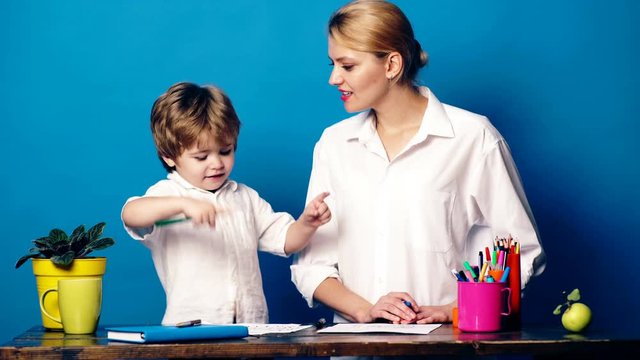 Young woman with a little boy painted with colored pencils and emotionally communicate on a blue background. Mom and son paint and communicate on a blue background. Learning concept.