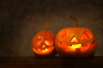 Two Halloween pumpkins glowing with bright light from inside, carved into creepy & funny Jack o Lantern in dark mystical atmosphere. Party decoration attributes. Background, copy space, close up.