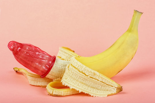 Red condom on yellow banana, pink background.