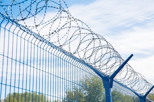 Blue fence with barbed wire on blue sky background. Dangerous area.