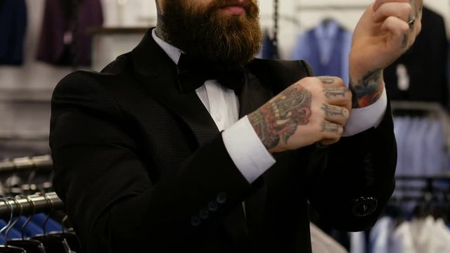 Close view of an elegantly dressed bearded man who trying on a suit while standing in a men's clothing store.