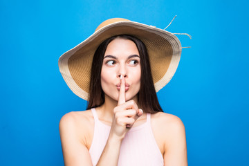 Portrait closeup of woman wearing straw hat showing finger at lips to keep secret isolated over blue background