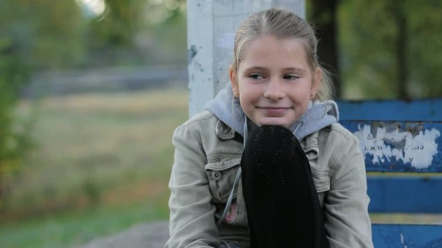 Cute preteen girl smiling sitting on old bench with her head on her knee