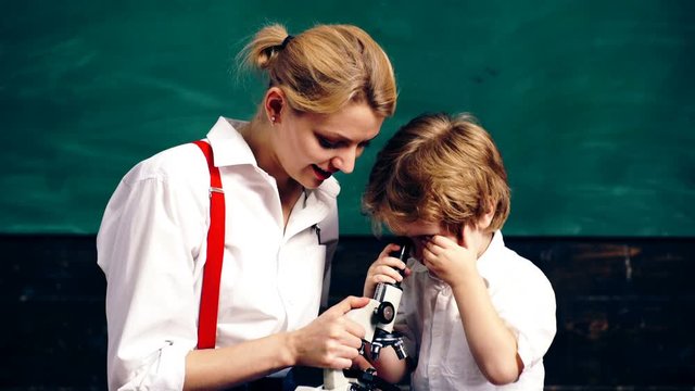 Young woman with a little boy looking at a wheat stem in a microscope on a green board background. Teacher and student. Back to school.