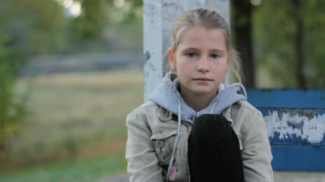 Pretty preteen girl child calm looking at camera sitting alone outdoors