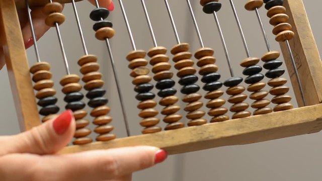 A girl is holding a vintage wooden abacus, performs a calculation on counter. Close-up.
