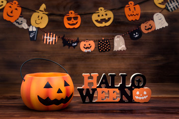 Front view of halloween decoration. In this photo, pumpkin bucket, a ornament writed halloween, mini flags and woonden background. Decoration, party, holiday and food as a concept