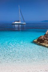 Beautiful calm azure blue lagoon with sailing catamaran yacht boat at anchor. Pure white pebble...