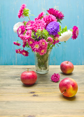 bouquet of garden flowers in a vase on a wooden table and apples