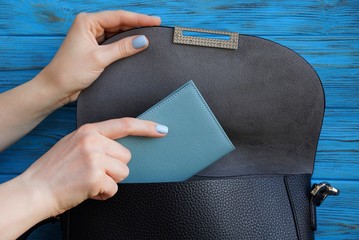 woman hand is laying a gray notebook in a black leather bag