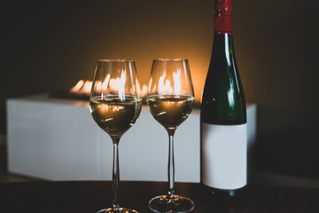 Two glass of white wine with green of bottle near the fireplace with copy space