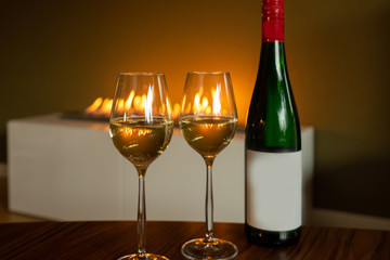 Two glass of white wine with green of bottle near the fireplace with copy space