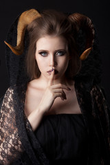 Portrait of an attractive demon woman with horns and curly hair, studio shot for Halloween
