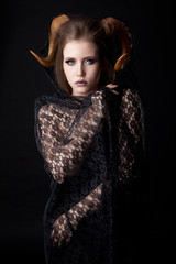 Portrait of an attractive demon woman with horns and curly hair, studio shot for Halloween