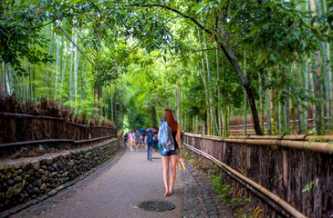 Beautiful girl carrying shoes walking in a public bamboo garden.
