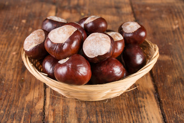 Chestnuts in beautiful retro basket on wooden desk. Autumn concept background. Close up, selective focus