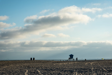 Lifeguard tower in the distance on a sandy beach below big billowy clouds.