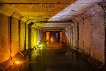 Flooded rectangular sewer tunnel with dirty urban sewage illuminated by color lights and candles 