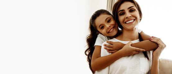 Family. Love. Togetherness. Portrait of happy mom and daughter hugging, looking at camera and smiling; at home - obrazy, fototapety, plakaty