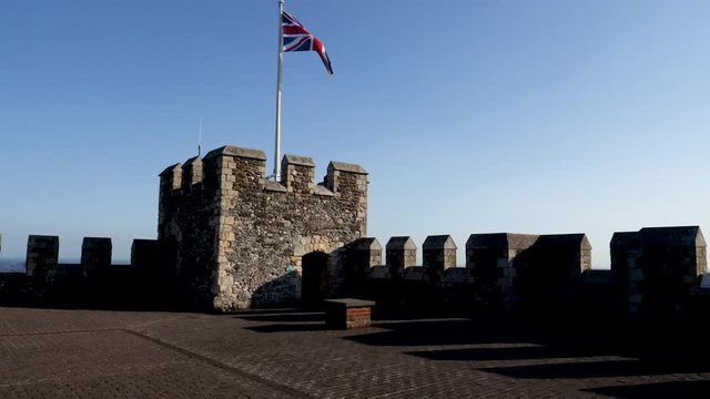 British flag, flag of the United Kingdom or Union Jack  waves over ramparts of Dover Castle as dark shadows fall in the late afternoon light.