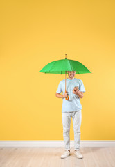 Man with green umbrella and smartphone near color wall