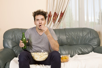 Excited young man with the remote and popcorn on the couch watching tv