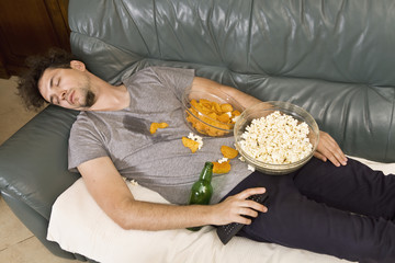 A man sleeping on a couch in a mess of junk food
