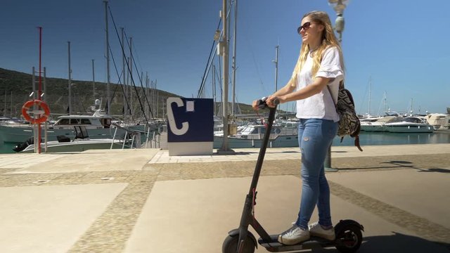 Full shot - Female riding electric scooter through marina