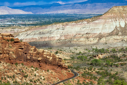 Afternoon light on the steep, sloping bluffs of the eastern side of Colorado National Monument, Rim Rock Drive, the town of Grand Junction, and distant mountains